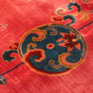 Close-up of a rug with a red field and an ornate central medallion in teal, brown, and coral colors.