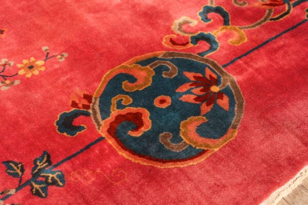 Close-up of a rug with a red field and an ornate central medallion in teal, brown, and coral colors.