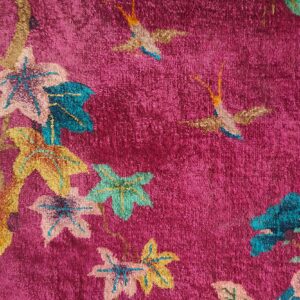 Textured pink rug with colorful leaves and birds in teal, gold, and pale pink, adjacent to a wide gold border.
