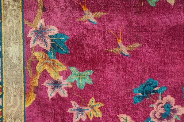 Textured pink rug with colorful leaves and birds in teal, gold, and pale pink, adjacent to a wide gold border.