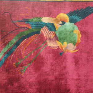 Textured magenta rug displaying a stylized multicolored bird with flowing tail feathers and a border.
