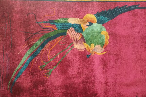 Textured magenta rug displaying a stylized multicolored bird with flowing tail feathers and a border.