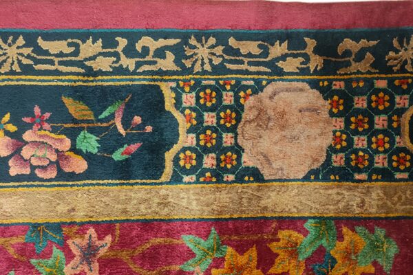 Ornate rug border featuring floral motifs and geometric patterns in deep magenta, teal, and gold.