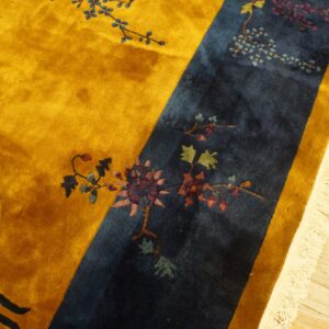 Gold and indigo rug featuring intricate floral designs and visible high pile on a light wood floor.
