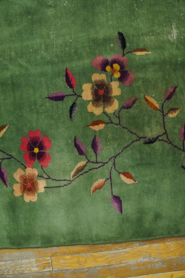 Low-pile green rug with multicolor floral and vine pattern resting on worn yellow wood planks.