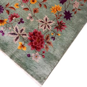 Corner of a distressed green low-pile rug with a detailed pattern of large flowers in burgundy, purple, and yellow.