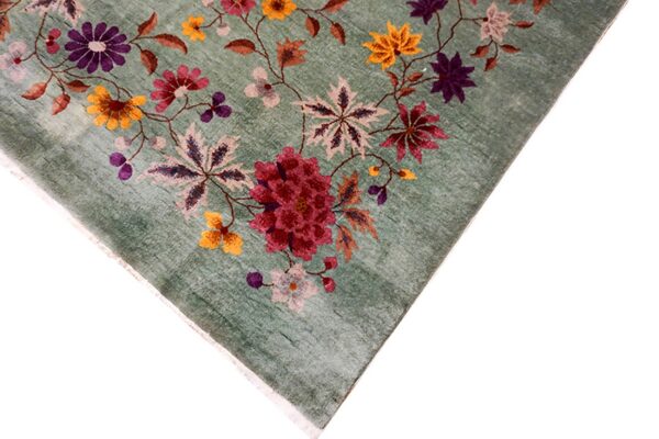 Corner of a distressed green low-pile rug with a detailed pattern of large flowers in burgundy, purple, and yellow.