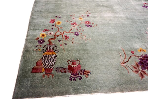 Muted green rug detailed with colorful blossoming branches, ornate vases, and decorative objects.