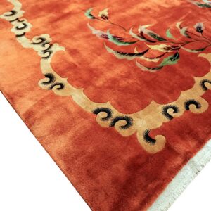 Orange high-pile rug detail showing a stylized gold scalloped border and variegated floral pattern.