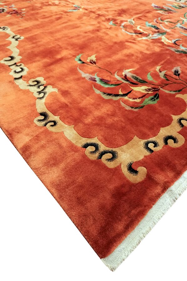 Orange high-pile rug detail showing a stylized gold scalloped border and variegated floral pattern.
