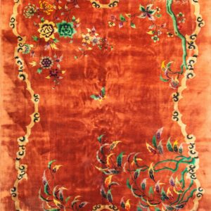 A lustrous, reddish-orange rug features a gold scalloped border and colorful floral and vine patterns.