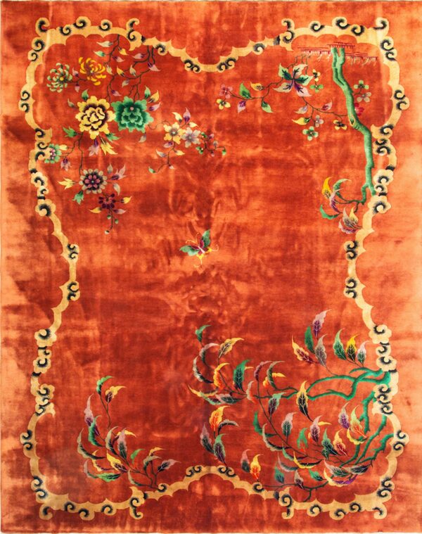 A lustrous, reddish-orange rug features a gold scalloped border and colorful floral and vine patterns.