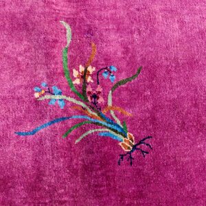 Vibrant magenta rug detail with plush pile, showing a multicolored floral motif and blue and pink borders.