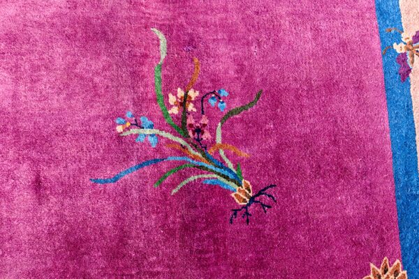 Vibrant magenta rug detail with plush pile, showing a multicolored floral motif and blue and pink borders.