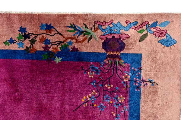 High-pile rug corner detail in magenta and pink with a blue border, featuring stylized leaves and floral branches.