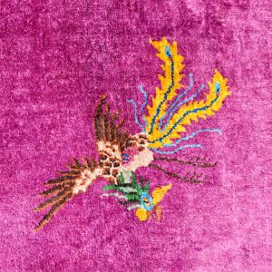 High-pile magenta rug featuring a stylized avian design with contrasting yellow, blue, and brown accents.