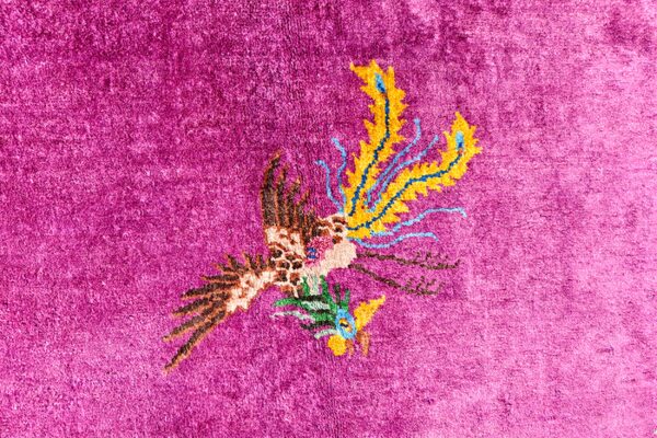 High-pile magenta rug featuring a stylized avian design with contrasting yellow, blue, and brown accents.