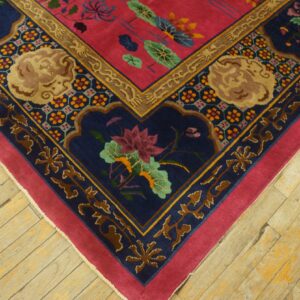 Close-up of a colorful rug corner featuring pink, navy, and gold floral patterns on worn wood planks.