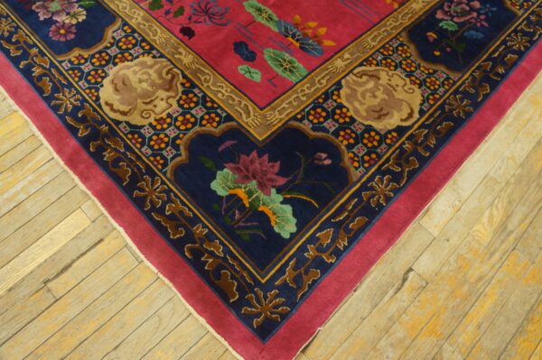 Close-up of a colorful rug corner featuring pink, navy, and gold floral patterns on worn wood planks.
