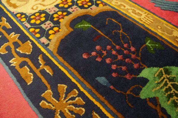 A dense pile rug displays botanical motifs in deep blue, gold, green, and pink colors on a red floor.