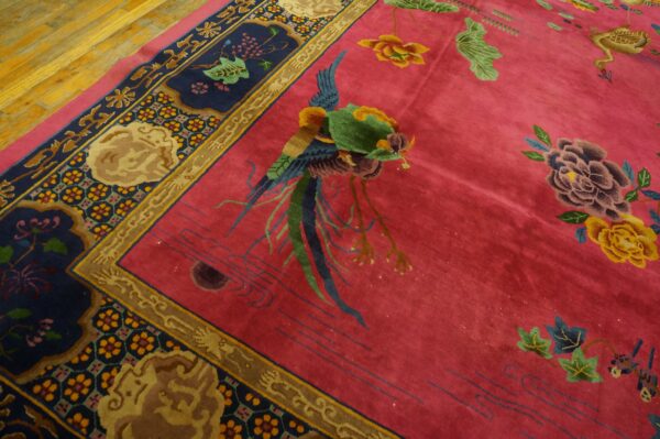 Diagonal view of a magenta rug with a central avian design and elaborate navy floral borders on wood floor.