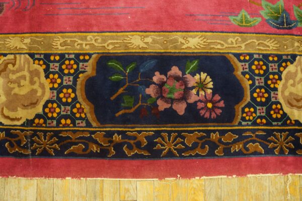 Close-up of a pink rug with ornate navy blue and gold floral borders over wood floors.