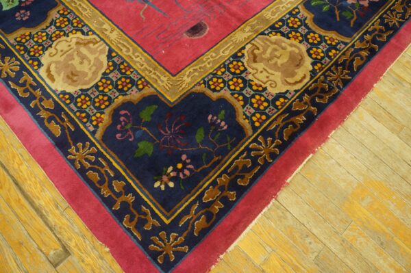 Ornate pink and navy rug corner with gold and floral motifs sits on worn yellow wood planks.