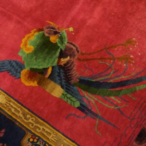 Red patterned rug featuring a stylized green and navy blue bird against a crimson field.