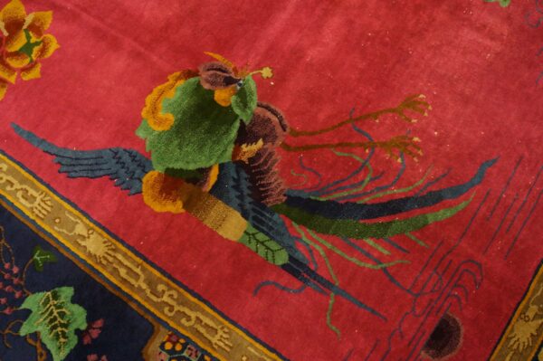 Red patterned rug featuring a stylized green and navy blue bird against a crimson field.