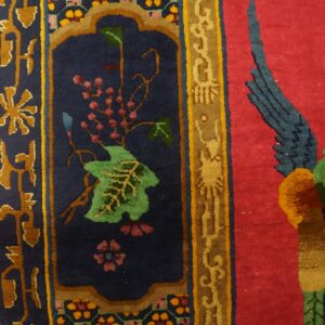 Red and navy rug detail with floral border designs, a green vine, and a large colorful bird motif.