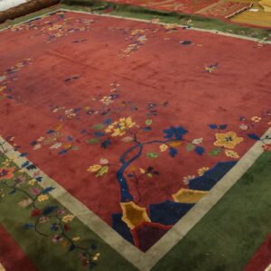Multicolored floral rug with a deep red field and broad olive green border rests on light wood flooring.