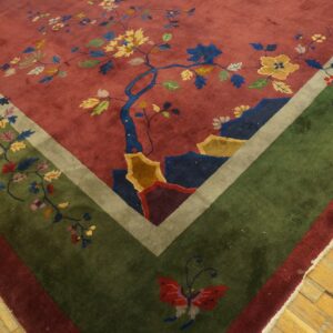 Plush rose and green rug featuring detailed multicolored florals and a butterfly, resting on worn wood flooring.