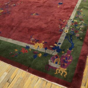 Deep red rug with a wide green border and colorful floral designs rests on distressed yellow hardwood flooring.