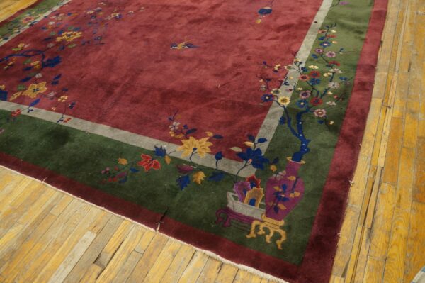 Deep red rug with a wide green border and colorful floral designs rests on distressed yellow hardwood flooring.