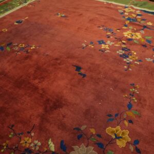 Close-up of a rust-colored rug with scattered floral branches, birds, and wide green and gray borders.
