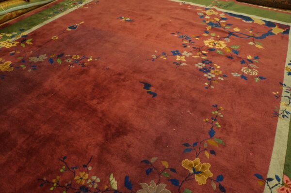 Close-up of a rust-colored rug with scattered floral branches, birds, and wide green and gray borders.