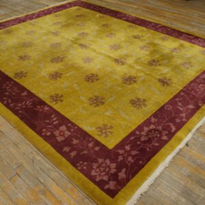 Yellow rug with scattered floral pattern and wide burgundy border rests on worn wood flooring.