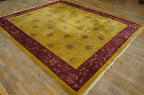 Yellow rug with scattered floral pattern and wide burgundy border rests on worn wood flooring.