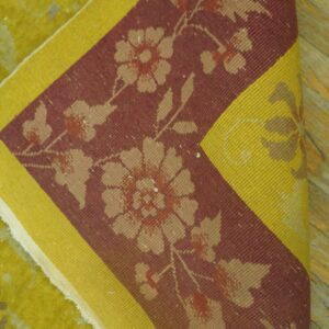 Folded rug showing chartreuse high-pile field, and a burgundy border with beige florals and a yellow stripe.