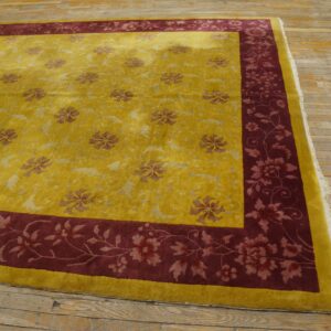 Golden yellow rug with a burgundy floral border sits on distressed, wide-plank wood floors.
