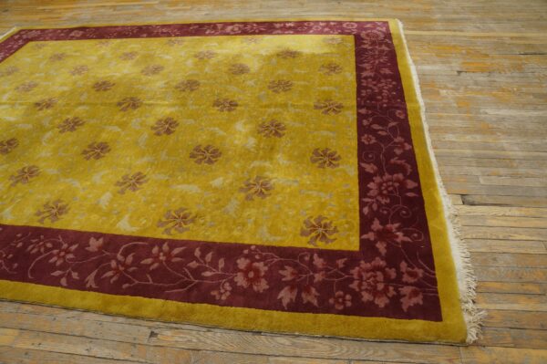 Golden yellow rug with a burgundy floral border sits on distressed, wide-plank wood floors.