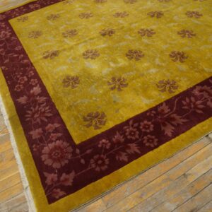 Yellow floral rug with a deep red border, fringe, and sheen rests on worn light wood flooring.