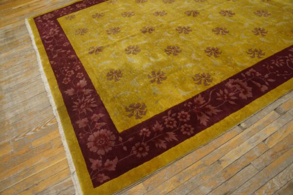 Yellow floral rug with a deep red border, fringe, and sheen rests on worn light wood flooring.