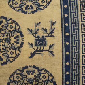 Cream rug with blue medallions and floral designs and a patterned border on wood flooring.