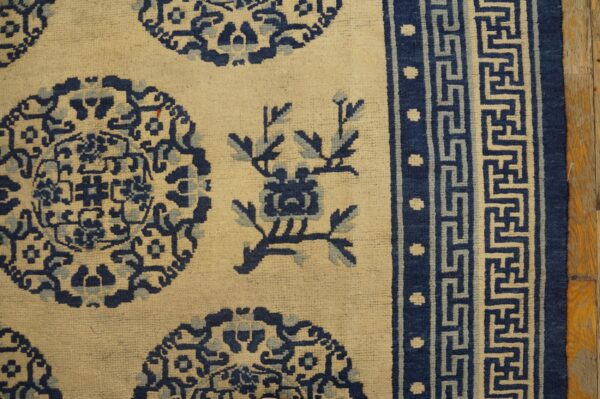 Cream rug with blue medallions and floral designs and a patterned border on wood flooring.