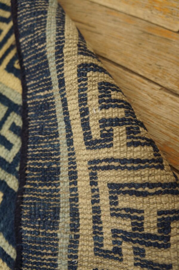 Detail shot of a coarsely woven tan and blue geometric rug resting on wood floorboards.