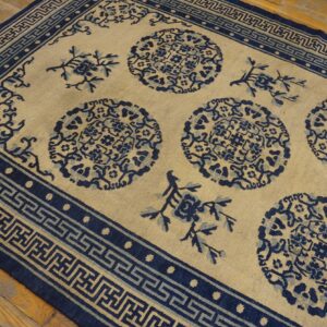 Light beige rug with navy and light blue medallion patterns and a Greek key border on wood planks.