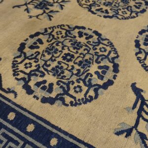 A detailed low-pile rug features dark and light blue medallions and a key pattern on a beige field.