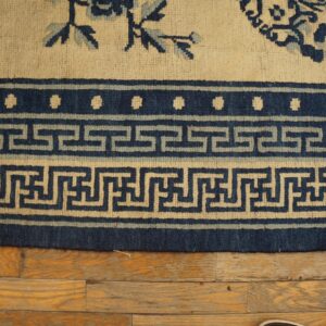 Detail of a cream and blue rug border with Greek key pattern resting on distressed wood planks.