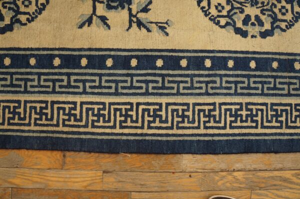Detail of a cream and blue rug border with greek key pattern resting on distressed wood planks.